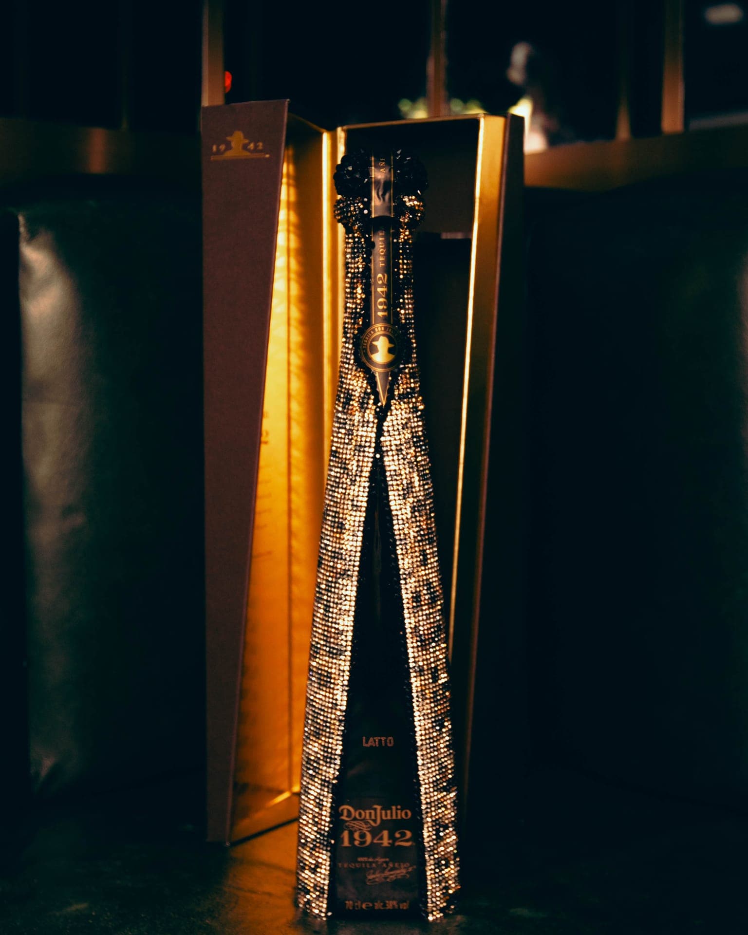 A crystal-embellished tequila bottle standing in an open gold presentation box